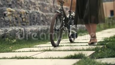 女人的腿在城市道路上骑自行车旁行走。 女子脚和自行车轮
